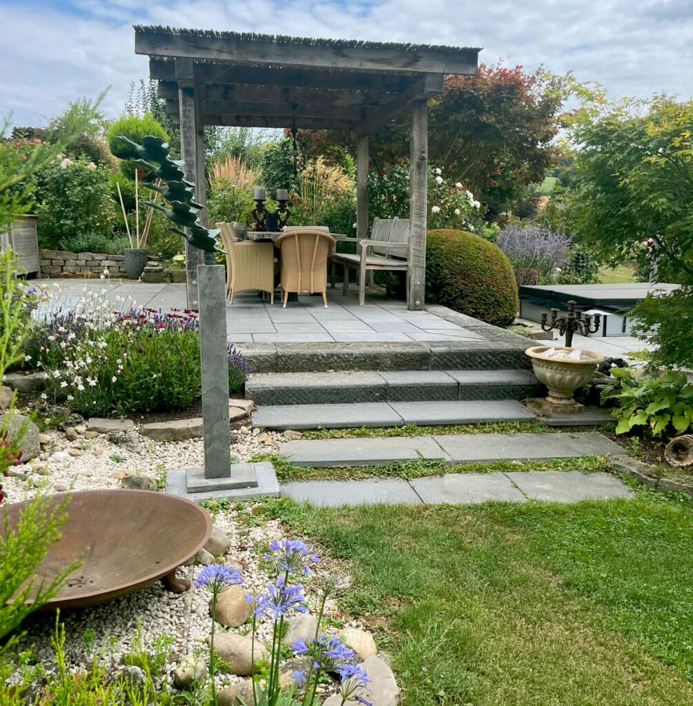 Überdachte Gartenterrasse mit Gartenmöbeln und Feuerschale